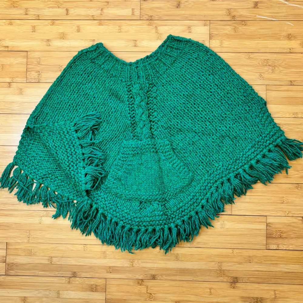 Hand knit fringed girl’s poncho. Cables centered on front and back, front pouch.